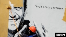 Работник заличава с боя графит, изобразяващ руския опозиционер Алексей Навални, в Санкт Петербург, Русия, 28 април 2021 г. Графитът гласи: "Герой на новото време".