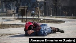 O mamă își acoperă fiul în timp ce stă întins pe un pământ după ce a auzit bombardamente în timpul conflictului dintre Ucraina și Rusia, în portul din sudul asediat Mariupol, Ucraina, 23 martie 2022.